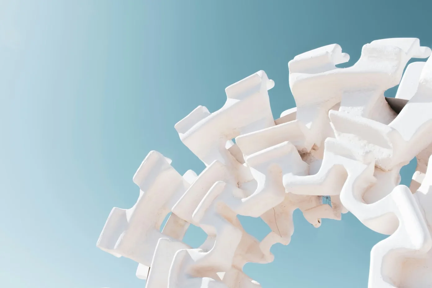 A professional photograph showing abstract white interlocking architectural elements or sculptural pieces against a clean light blue sky background.